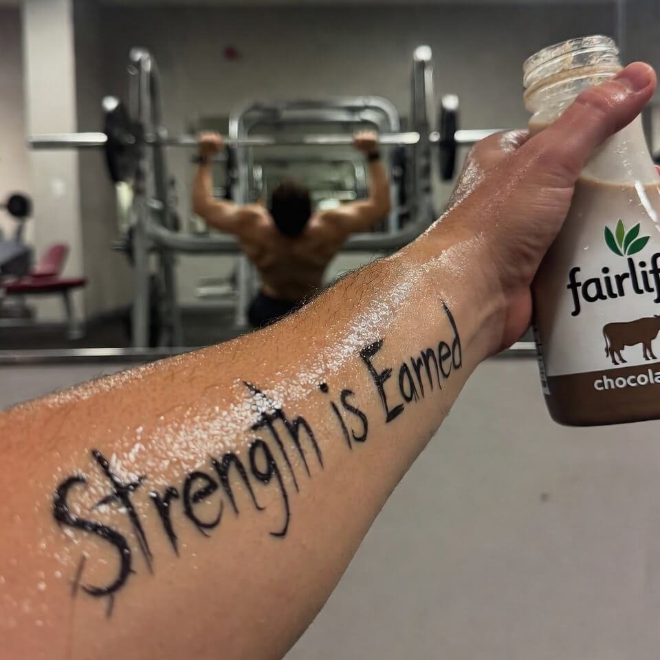 Sweaty forearm tattoo holding chocolate milk in gym mirror