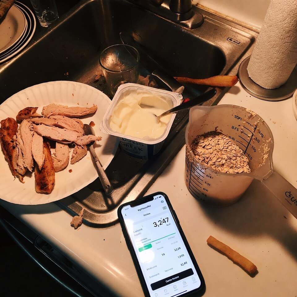 Chaotic kitchen counter with chicken, yogurt, and calorie tracker